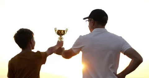 Father and son hold trophy at sunset with proud smiles. Trophy shines in golden Stock Footage 316755782