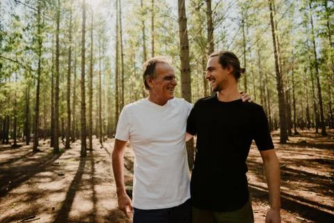 Father and son hugging while smiling at each other standing in green forest. Stock Photos