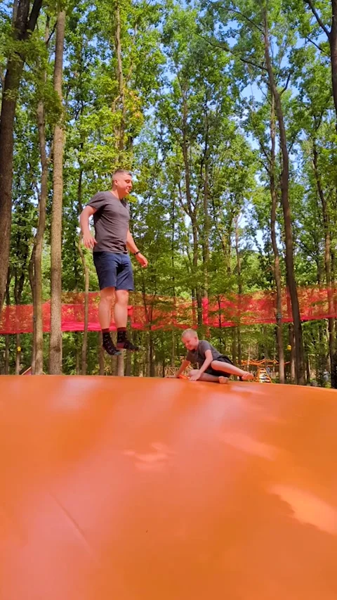 Father and son jumping on giant inflatable jumping pillow at outdoor amusement p Stock Footage 342714357