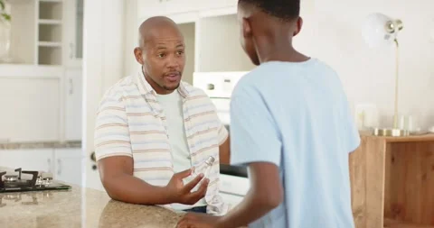 Father and son at kitchen island, father showing clear bottle, explaining, son Video stock 344851589