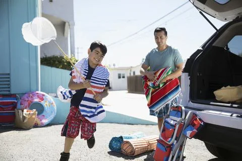 Father and son loading car for beach trip in sunny driveway Stock Photos