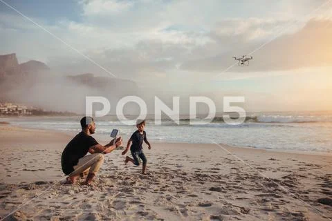 Father and son playing with flying drone on beach Stock Photos