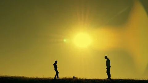 Father and son playing football in the park at sunset, silhouettes against the Stock Footage