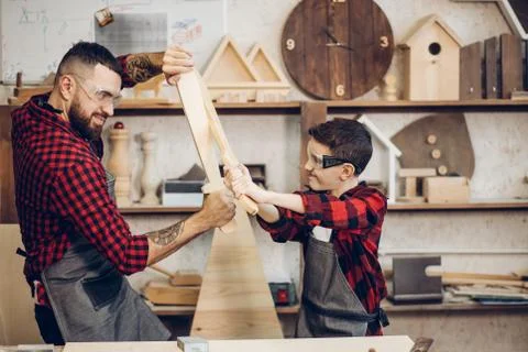 Father and son playing knights with wooden DIY swords at carpenter workshop Stock Photos