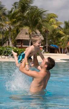 Father and son playing in outside swimming pool at a tropical resort Stock Photos