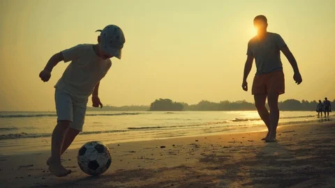 Father and son playing together with ball in football on the beach under sunset Stock Footage 87708361
