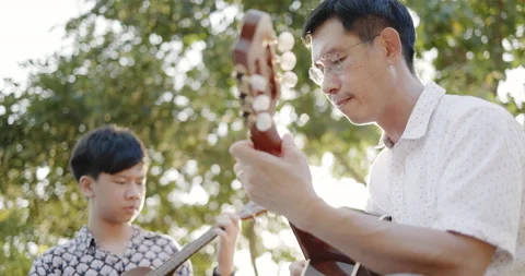 Father and son practice playing guitar with enthusiasm, happy relaxing  Vidéo 166906423