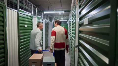 Father and Son Pulling Cart Loaded with Boxes through Storage Corridor Video stock 327782542