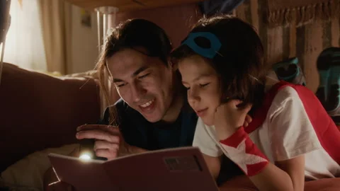 Father and Son Reading Bedtime Story with Flashlight in Blanket Fort Stock Footage 336177449
