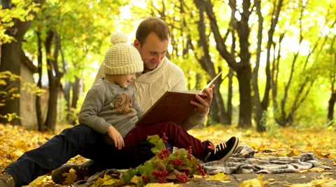 Father and son reading book in yellow autumn park Stock Footage 68955954