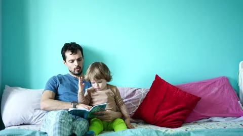 Father and son reading together on a sofa before bedtime Stock Footage 329405387