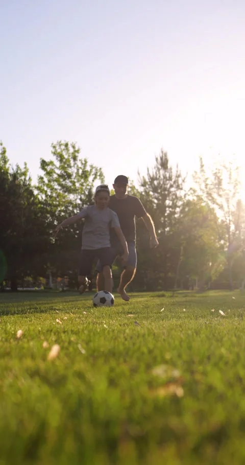 Father and son run barefoot through park at sunset, playfully competing for Stock Footage 346753365
