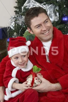 Father And Son In Santa Claus Outfit Holding Present Stock Photos