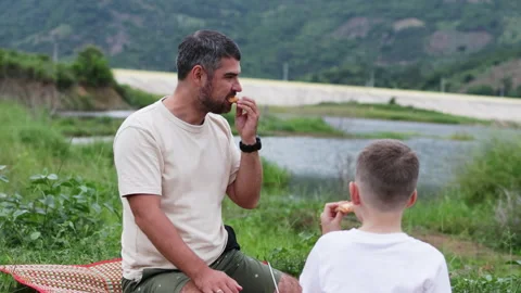 Father and son share laughter and pizza during joyful picnic. Stock Footage 288422626