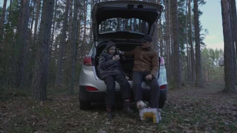 Father and son sitting inside car trunk and drinking tea from thermos. Stock Footage 164985102