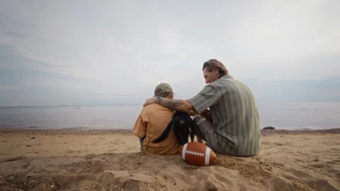 Father and Son Sitting on Sandy Beach Petting Black Dog Stock Footage 340255545
