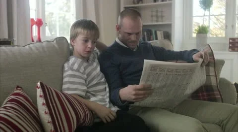 Father and son sitting in a sofa reading a newspaper Video stock 11289359