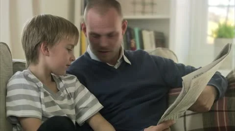 Father and son sitting in a sofa reading a newspaper Stock Footage 11289373