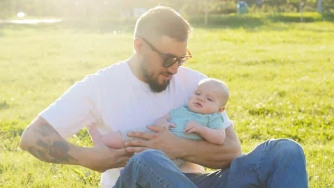 Father and son sitting together on the grass in summer evening sunset Stock Footage