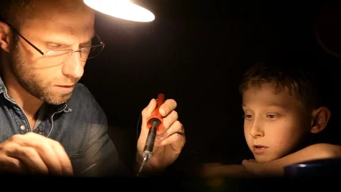 Father and son sitting under lamplight and soldering parts together Stock-Footage 105932019