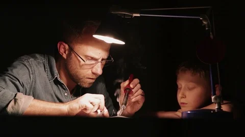Father and son sitting under lamplight and soldering parts together. Smoke lifti Stock-Footage 112226785