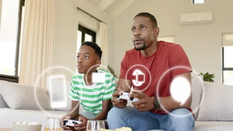 Father and son on sofa holding controllers UI mail or upload icons appearing Stock Footage 332981653