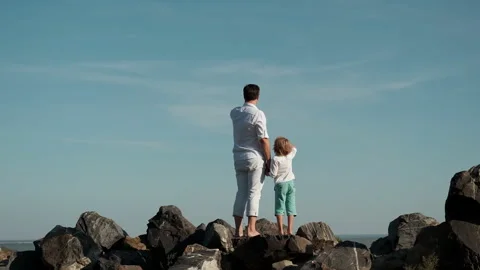 Father and son stand on the edge of a cliff and look at the ocean. Video stock 248895844
