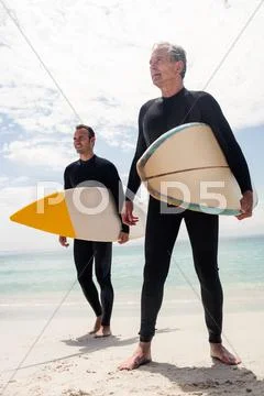 Father and son standing on the beach with surfboard and looking at a distance Stock Photos