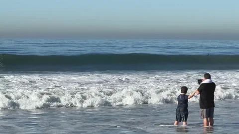Father and Son Standing in Waves on Beach Stock Footage 228890519