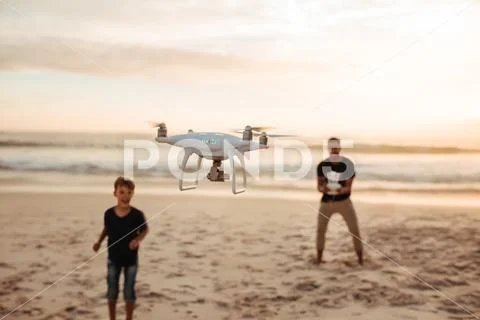 Father and son on summer vacation flying drone on beach Stock Photos