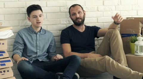 Father and son talking while sitting on floor at their new home Stock Footage 63055786