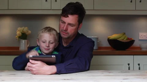 Father and son use an electronic tablet at the kitchen table Stock Footage 62545120