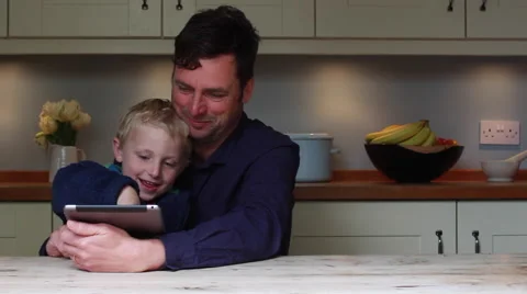 Father and son use an electronic tablet at the kitchen table Stock Footage 62545141