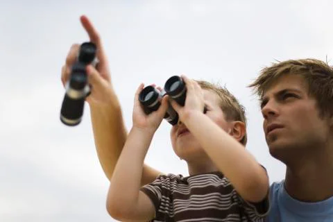 Father and son using binoculars, man pointing skyward Stock Photos