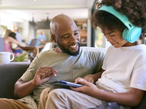 Father And Son Using Digital Tablet With Headphones At Home With Stock Photos