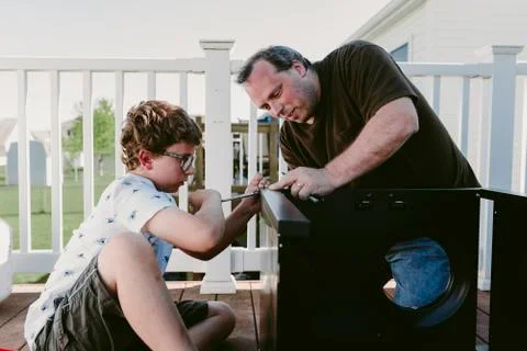 Father and son using screw driver while making metallic cabinet on porch Foto stock