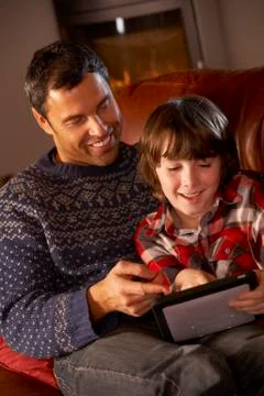 Father And Son Using Tablet Computer By Cosy Log Fire Stock Photos