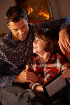 Father And Son Using Tablet Computer By Cosy Log Fire Stock Photos