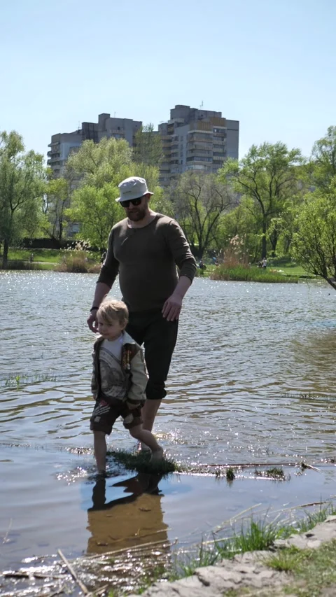 A father and son walk through the shallows of a river on a sunny spring day. Stock Footage 338305229