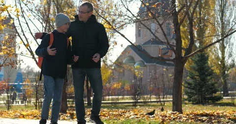 Father and son walk through autumn park, happily talking and sharing a joyful Stock Footage 343856216