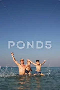 Father and sons playing in the ocean Stock Photos