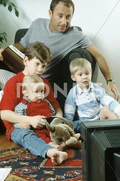 Father and three sons watching TV together Stock Photos