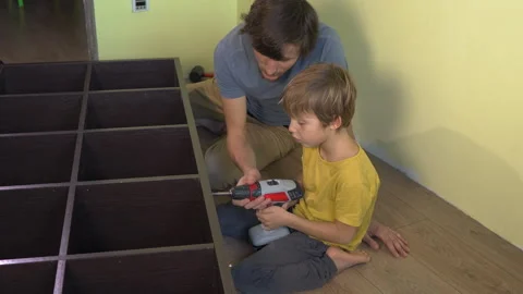 Father and young son build a large bookshelf together using an electric Video stock 325662860