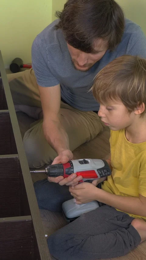Father and young son build a bookshelf together using an electric screwdriver Video stock 332564862