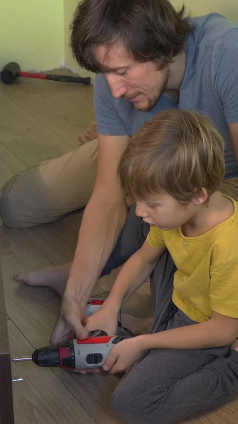 Father and young son build a bookshelf together using an electric screwdriver Video stock 332565170