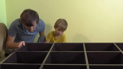 Father and young son build a large bookshelf together using an electric Video stock 336564563