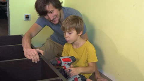 Father and young son build a large bookshelf together using an electric Video stock 336565309