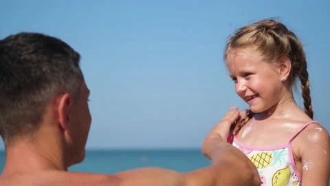 Father applying protective cream to her daughter's face at the beach. Stock Footage 173515089