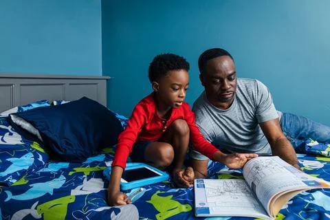 Father assisting son studying in bedroom at home Stock Photos