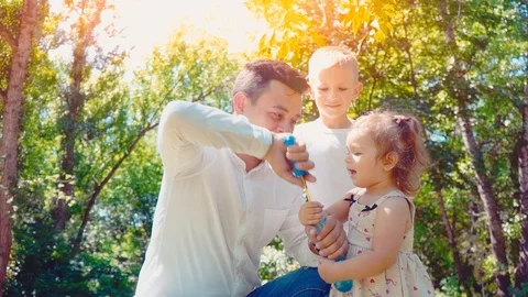 Father blowing soap bubbles for son and little daughter in the park, lifestyle Stock Footage 90982394